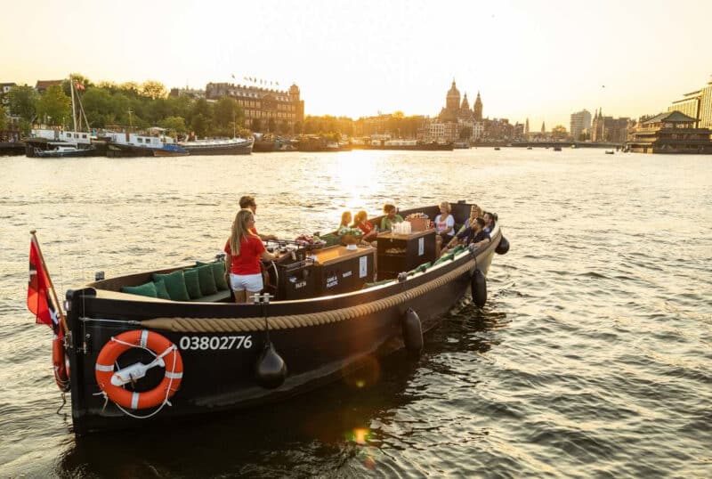 Barco abierto con patrón al atardecer en los canales de Ámsterdam